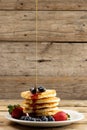 Vertical image of maple syrup pouring onto pancakes and blueberries, on wood with copy space Royalty Free Stock Photo