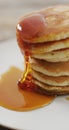 Vertical image of maple syrup pouring onto stack of american style pancakes