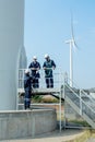 Vertical image one technican worker give the document to his coworker stand in base of windmill or wind turbine