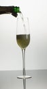 Vertical image of open bottle pouring champagne into single tulip glass on white background