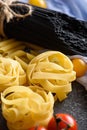 Vertical image of pasta - black spaghetti, fettuccine, tomatoes on gray background