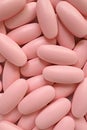 Vertical image of pile of pastel pink oval shaped pills for background or banner