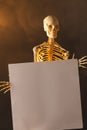 Vertical image of plastic skeleton holding paper sheet and smoke with copy space on black background