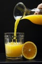 Vertical image.Pouring orange juice.Flass bottle and glass full of orange juice, slice of orange against dark background
