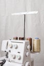 Vertical image.Professional overlock machine and spool of threads agaisnt white fabric background