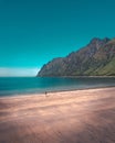 Vertical image of a shore with mountains on the left and a person walking on the beach Royalty Free Stock Photo