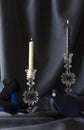 Vertical image.Still life image, old fashioned styye.Candle flames, white and black candle, glass candkesticks, dark blue curtains