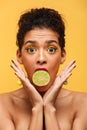 Vertical image of surprised afro american woman bulging eyes while putting half of fresh lime in mouth isolated, over yellow back Royalty Free Stock Photo