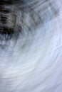 Conceptual image of blue and white skies with darker tree limbs in swirling lines, a photo technique known as panning