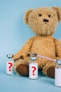 Vertical image of teddy bear with unnamed vial dose of vaccine or another medicine with syringe against blue background with copy Royalty Free Stock Photo