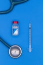 Vertical image of a top view of a COVID-19 vaccine vial with a syringe and stethoscope on a blue background