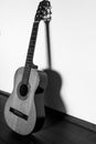 Vertical image of an used, old, cracked classic guitar with dark shadow on the white wall Royalty Free Stock Photo