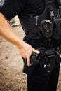 Vertical image of white male caucasian police officer reaching down and places hand on his weapon hand gun that is still in its Royalty Free Stock Photo