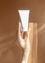 Vertical image of woman& x27;s hand holding mock-up of white plastic cream tube in rays of sunlight. Container for Royalty Free Stock Photo