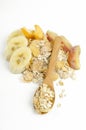 Vertical image.Wooden spoon, heap of oatmeal, corn flakes, pieces of banana, peach, plum on the white surface.Delicious ingredient