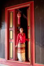 Vertical image of young Asian woman with Thai Lanna traditional dress stand at door with red color and old style of ancient house Royalty Free Stock Photo