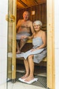 Vertical indoor shot of married couple enjoying sauna. Caucasian senior woman in gray towel touching the knee of her Royalty Free Stock Photo