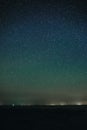 Vertical landscape of bright starry night sky with lights upon on it and sandy empty beach with grass and ocean