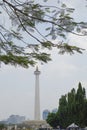 Vertical lateral image of Jakarta National Monument on a sunny day behind some tree branches