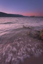 Vertical long exposure of foamy sea waves hitting the shore line and showering a driftwood at sunset Royalty Free Stock Photo