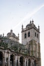 Low-angle shot of the tower of the Porto Cathedral on a bright day, with birds flying in the sky.