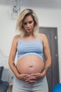 vertical medium shot of a blond pregnant woman at home