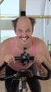 Vertical, medium shot, funny bald man is training on an exercise bike, smiling