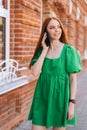 Vertical medium shot portrait of happy young woman talking on mobile phone walking on city street in summer day. Royalty Free Stock Photo