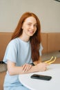 Vertical medium shot portrait of smiling young woman holding in hands yellow stylish sunglasses sitting at table in cafe