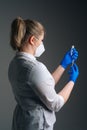 Vertical medium studio shot of nurse in blue gloves and face mask holding and filling up vaccine to syringe on black