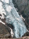 Vertical mountain landscape with blue long vertical glacier tongue with cracks among rocks. Aerial view to large glacier with