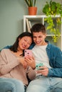 Vertical. Multiracial married couple using a cellphone to search apps sitting on living room sofa. Young people smiling Royalty Free Stock Photo