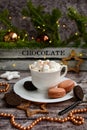 Vertical New Year composition. Coffee with mashmelou in a white cup, macarons, brown beads, stars on the background of glowing