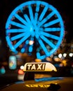 Vertical shot of a taxi sign in front of an illuminated ferris wheel in downtown Cologne, Germany