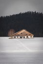 Vertical of an old rustic wooden house situated in a snowy field against green mountains Royalty Free Stock Photo
