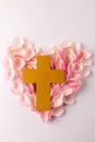 Vertical overhead of yellow christian cross on heart of pink rose petals, on white with copy space Royalty Free Stock Photo