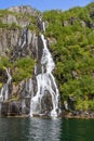 Rushing waterfall cascades over dark rocks among greenery in Trollfjorden Royalty Free Stock Photo