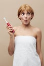 vertical photo on a beige background of a happy, funny woman holding a red, electric toothbrush in her hand, funny Royalty Free Stock Photo
