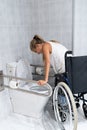 Vertical photo of a blonde girl getting up with her arms from a wheelchair in a toilet Royalty Free Stock Photo