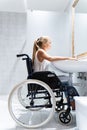 Vertical photo of a blonde girl sitting in a wheelchair in a bathroom