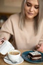 Vertical photo of blurred blond smiling woman pouring milk cream in coffee, eating brownie cake. Cafe holiday pleasure Royalty Free Stock Photo