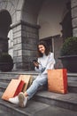 Vertical photo of brunette young woman sitting down on the stairs in the city with paper shopping bags around her Royalty Free Stock Photo