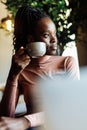 Vertical photo calm, dreaming african afro american young woman with dreadlocks, drinking coffee in cafe. Coffee break