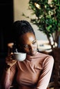 Vertical photo calm, dreaming african afro american young woman with dreadlocks, drinking coffee in cafe. Coffee break