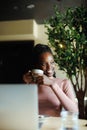 Vertical photo calm, dreaming african afro american young woman with dreadlocks, drinking coffee in cafe. Coffee break