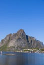 Vertical photo capturing Reine with classic red Rorbu houses set against a majestic, rugged cliff in the Lofoten Islands, Norway