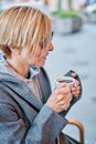 Vertical photo of Caucasian blonde woman wearing sunglasses sitting in a bar terrace with coat having a cup of coffee Royalty Free Stock Photo