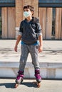 Vertical photo of a Caucasian boy with a mask, with skates in the park. New normal pandemic Covid 19