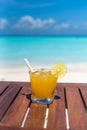 Vertical photo of Champagne Mango-lime aqua fresca cocktail with straw on wooden table ocean background at the beach