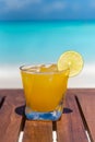 Vertical photo of champagne Mango-lime aqua fresca cocktail on wooden table ocean background at the beach